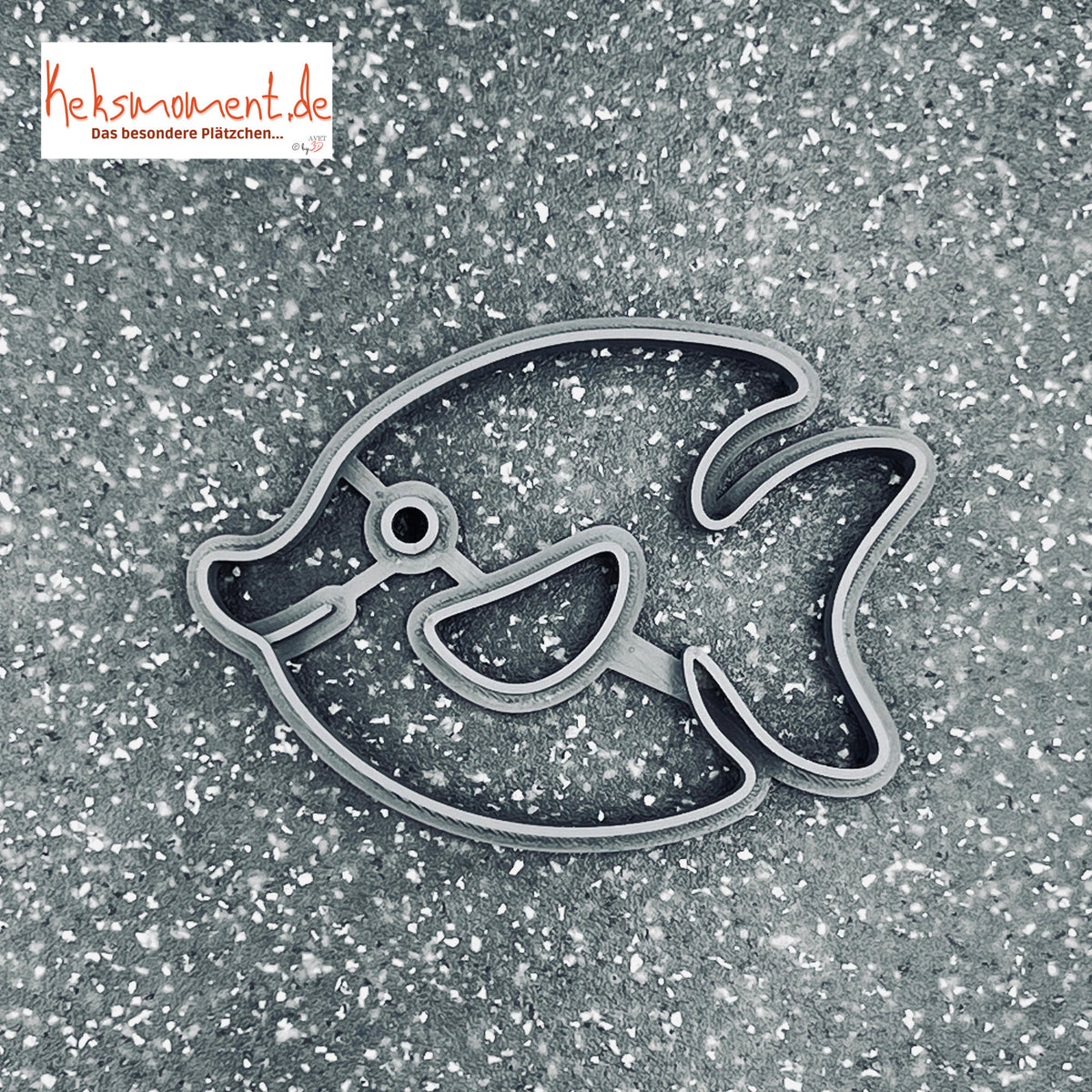 Fisch-Ausstecher auf dunklem, gesprenkeltem Untergrund; runde Augenlinie, lächelndes Maul und geteilte Schwanzflosse.