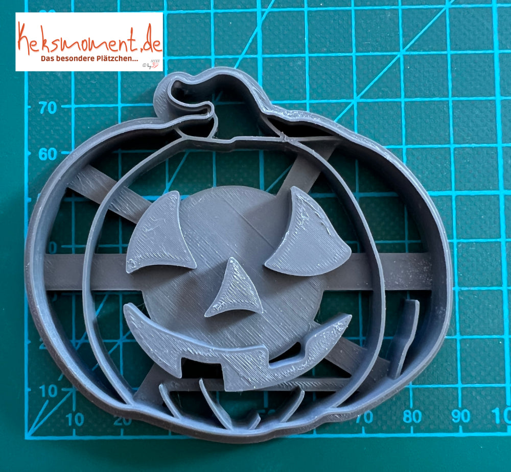 Halloweenkürbis-Ausstecher auf einer Schneidematte mit metrischer Skala zum Größenvergleich.