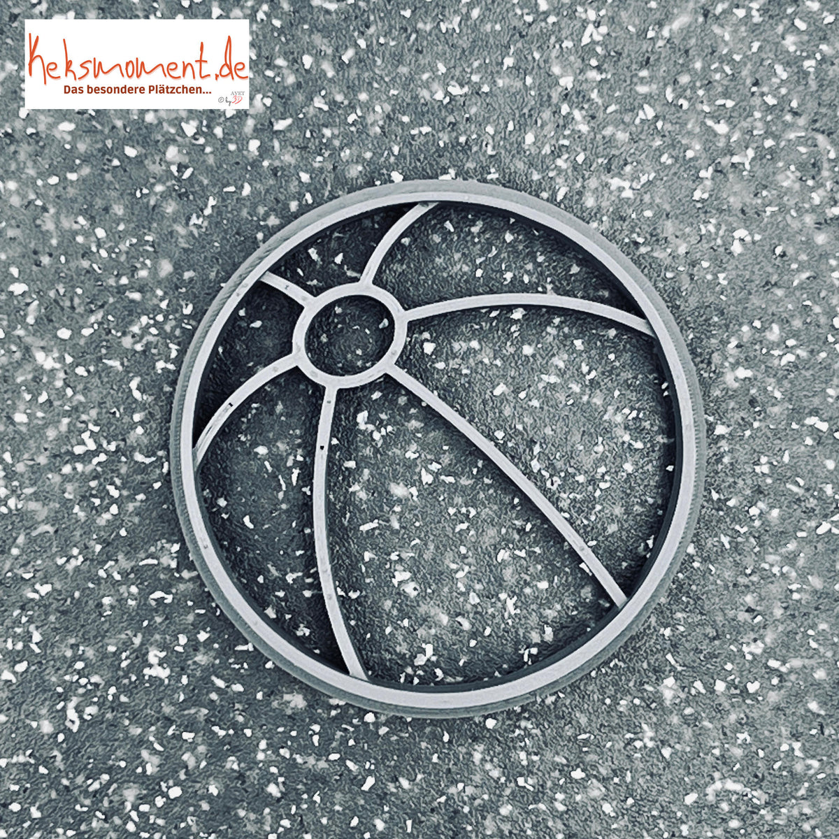 Wasserball-Ausstecher von oben auf dunkler Fläche mit kleinem Innenkreis und gebogenen Segmentstegen.
