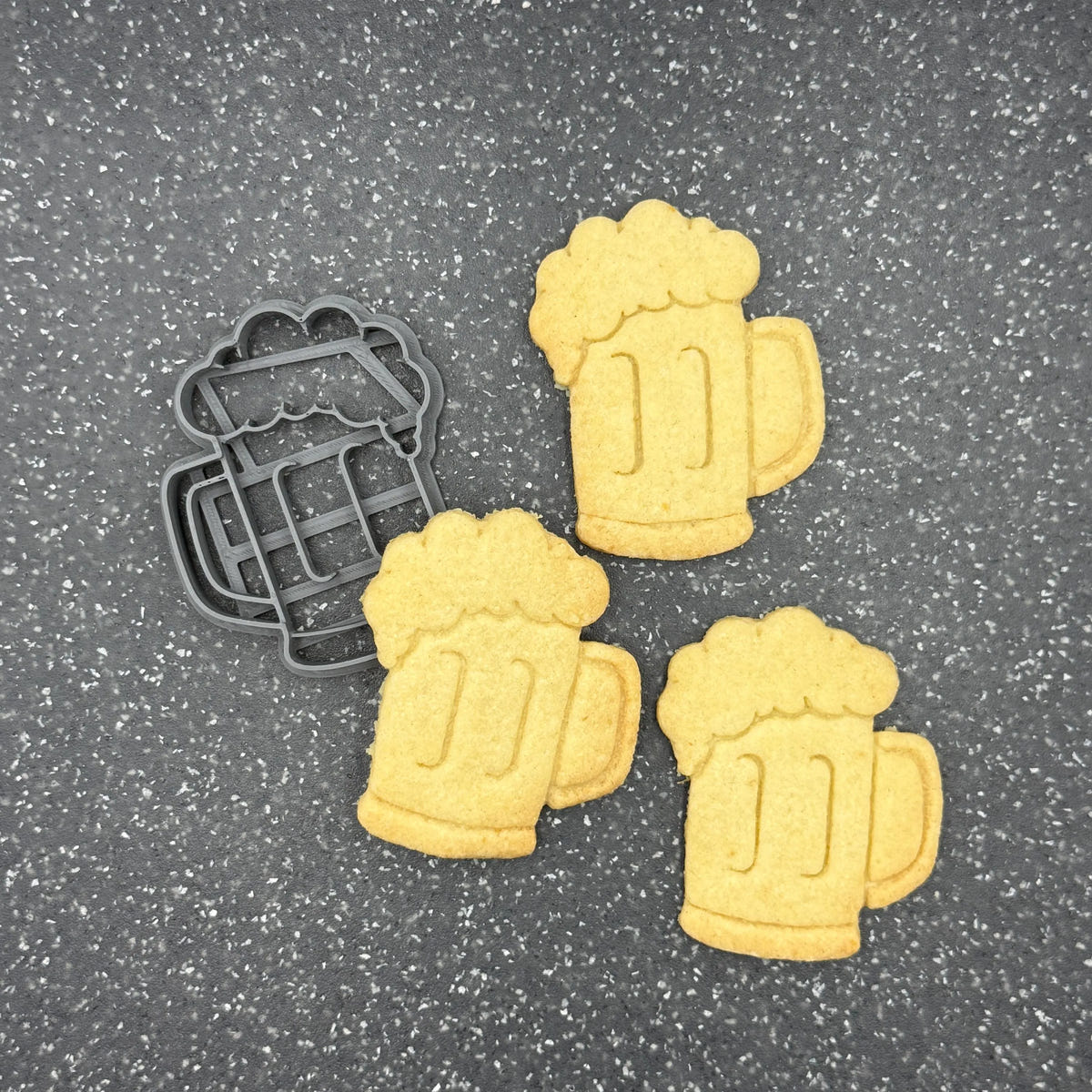Maßkrugausstecher neben drei gelblichen Krugmotiven mit Schaumkrone, Henkel und senkrechten Prägelinien auf dunkler Fläche.